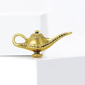 Golden Aladdin lamp brooch with vintage patterns displayed on white geometric blocks