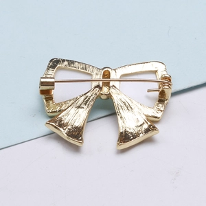 Detailed back view of a gold alloy bow brooch showing the safety pin clasp and texture