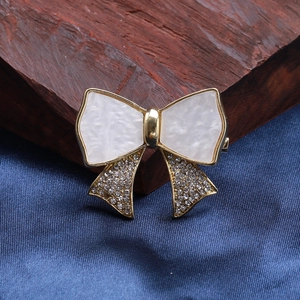 Macro detail of a gold bow brooch with marble inserts and shimmering crystal accents