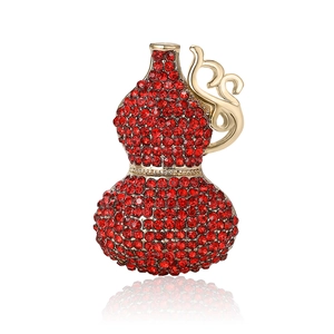 Luxurious gourd brooch with red rhinestones and gold accents on a white reflective base