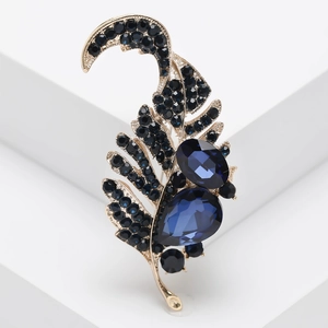 Elegant gold leaf brooch with deep blue rhinestones and crystals on white platform