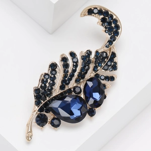 Vintage gold alloy feather brooch with deep blue crystals on a modern white stand