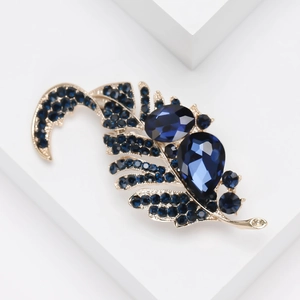 Macro shot of gold leaf brooch with deep blue rhinestones on a white minimalist block