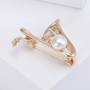 Détail de la broche saxophone dorée avec perle blanche sur support géométrique blanc