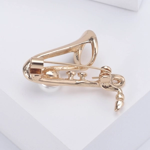 Élégante broche saxophone dorée avec perle sur fond blanc minimaliste de présentation