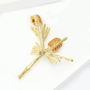 Detailed view of a gold pine branch brooch with sparkling amber cubic zirconia pinecones