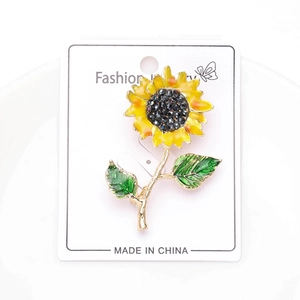 Gros plan d'une broche tournesol en émail jaune avec feuilles vertes et strass noirs