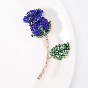 Dettaglio macro di un'elegante spilla a rosa blu con foglie in strass verdi e stelo dorato