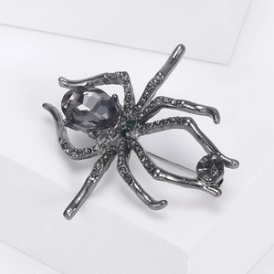 Macro detail of gothic spider brooch featuring dark grey crystals and green rhinestone eyes
