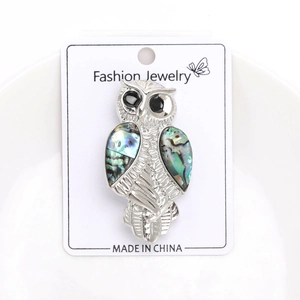 Detailed view of silver owl brooch with iridescent abalone shell wings on display card