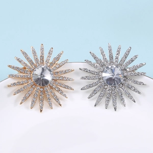 Dettaglio di spille a girasole con strass argento e oro su un piatto di ceramica bianca