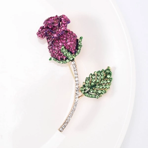 Dettaglio di spilla a rosa con cristalli rossi su un piatto bianco e finiture dorate