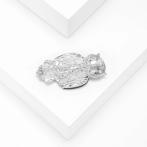 Silver owl brooch with shell inlay shown from the back on a white minimalist platform