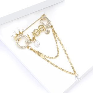 Macro shot of gold Queen letter brooch with crown detail, zircons and tassel chains