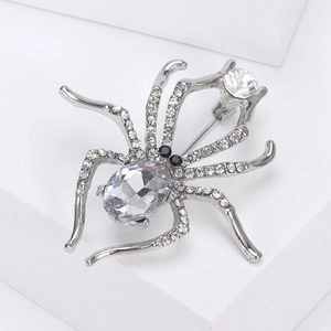 Macro shot of a silver spider brooch with clear rhinestones on white geometric props
