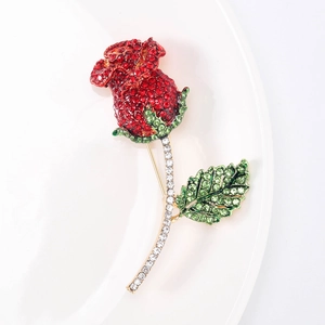 Dettaglio spilla a rosa con strass rossi e verdi su base in lega metallica dorata