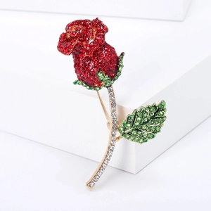 Elegante spilla a rosa dorata con strass rossi e verdi su supporto bianco moderno