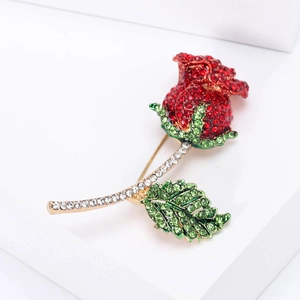 Dettaglio macro spilla a rosa con cristalli rossi e foglie verdi su base oro