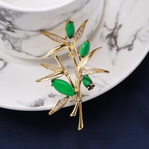 Elegante spilla a bambù con gemme verdi e zirconi bianchi su base in metallo dorato