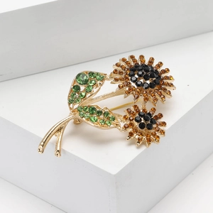 Elegant gold-tone sunflower brooch with amber and emerald rhinestones on white pedestal