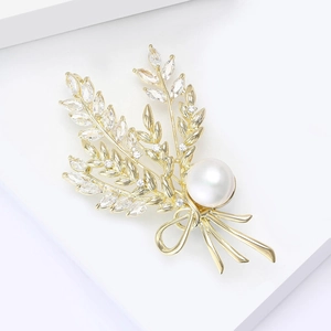 Vue détaillée d'une broche épi de blé dorée avec cristaux et perle sur support blanc