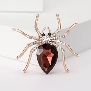 Macro detail of rose gold spider brooch with large red pear-cut gem and white crystals