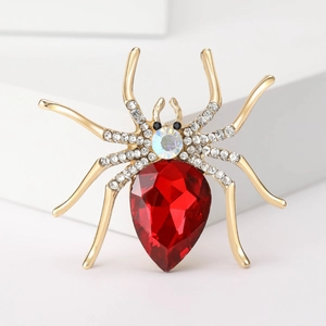Macro detail of golden spider brooch with large red teardrop gem and white rhinestones