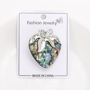 Macro detail of strawberry brooch featuring iridescent abalone shell and silver texture