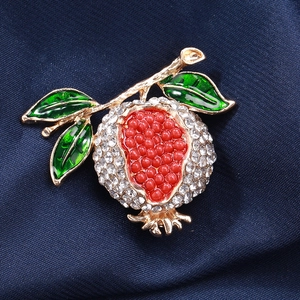 Détail macro d'une broche grenade avec perles rouges, feuilles vertes et zircons