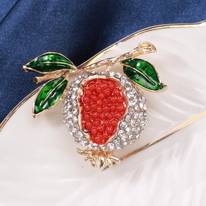 Vue macro d'une broche grenade avec perles rouges et strass sur une assiette en porcelaine
