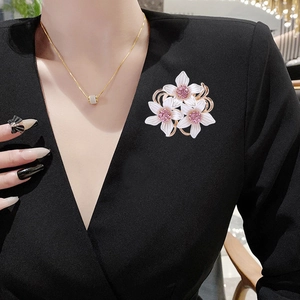 Élégante broche camélia dorée avec pétales blancs et cristaux roses sur une robe noire