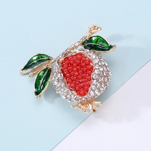 Détail de la broche grenade avec perles rouges, émail vert et strass blancs scintillants