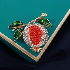 Détail d'une broche grenade avec perles rouges, strass blancs et émail vert