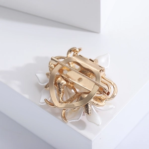 Vue arrière de la broche fleur dorée avec fermoir de sécurité sur socle blanc