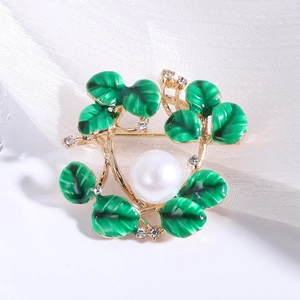 Detailed macro view of green enamel leaves and white pearl on gold floral brooch