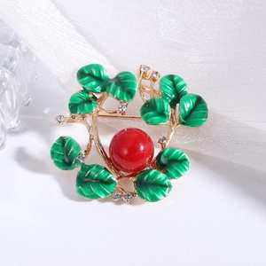 Detail of gold plant wreath brooch with green enamel leaves and red center bead