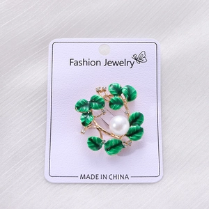 Detail view of floral wreath brooch featuring green enamel leaves and white pearl accent