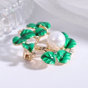Macro shot of green enamel leaves and white pearl on a golden plant-shaped brooch