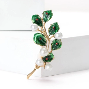Detail of leaf brooch with green enamel, white pearls, and gold finish on white stand