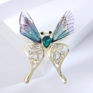 Detail of butterfly brooch with emerald drop stone and translucent wings on white background