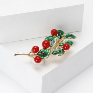 Elegant gold leaf brooch with red pearl berries and green enamel leaves on a white cube