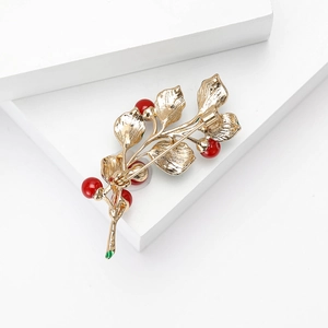 Detailed close-up of golden leaf brooch featuring red pearls and intricate metal vein textures