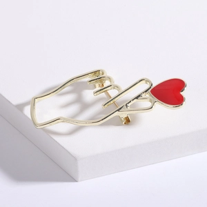 Vue macro d'une broche geste de main dorée avec un cœur en émail rouge et finitions soignées