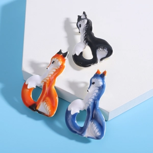 Detailed view of three colorful enamel fox brooches in orange, blue, and black-white