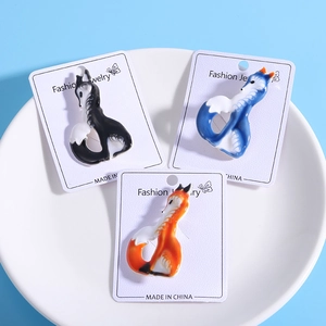 Close-up of enamel fox brooches in orange, blue, and black colors on white display cards