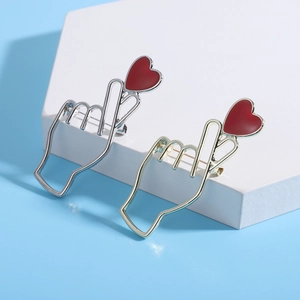 Détail de broches geste de cœur en or et argent avec émail rouge sur fond bleu clair