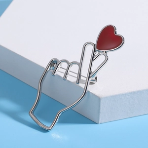 Broche main en forme de cœur argentée avec pendentif cœur rouge sur présentoir blanc