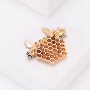 Broche creativo de abeja dorada y panal con esmalte ámbar sobre soporte blanco