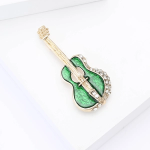 Detail of artistic gold guitar brooch with green enamel and sparkling rhinestones
