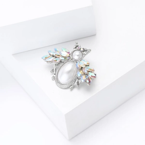 Macro shot of silver bee brooch with pearls and iridescent rhinestones on a white block